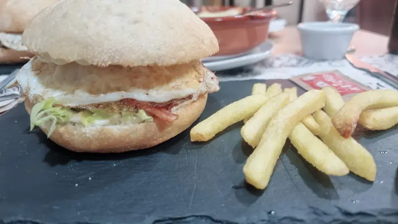 Hamburguesa con lechuga y patatas fritas servida sobre pizarra