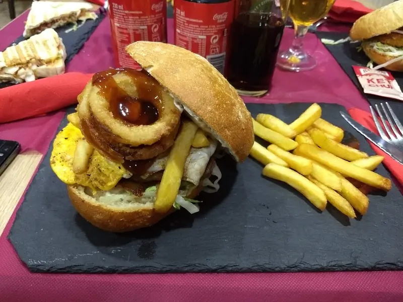 Hamburguesa con aros de cebolla y huevo, con patatas fritas sobre pizarra