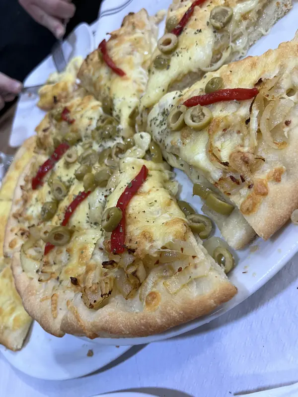 Pizza de masa media cortada en porciones, con cebolla, aceitunas y pimiento