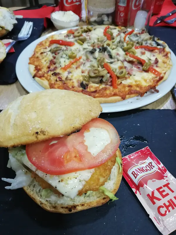 Pizza con pimiento y una hamburguesa de pollo crujiente en la misma mesa